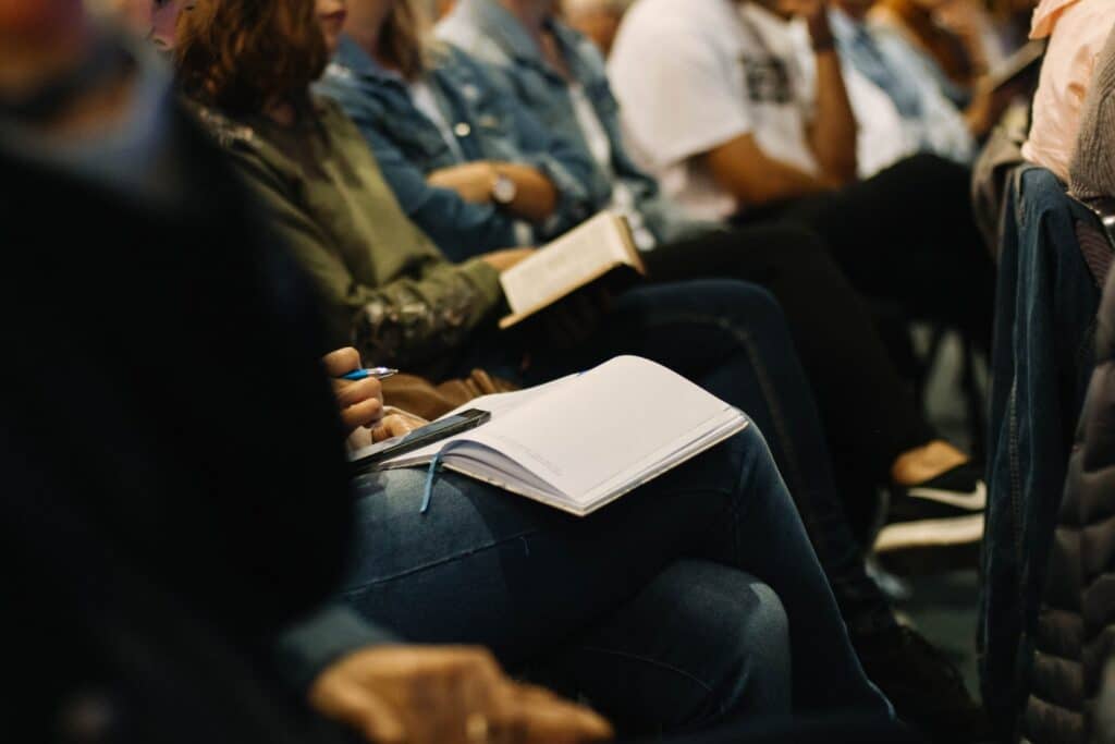 A photo of a row of people facing the same direction. A notebook sits open on somebody's lap