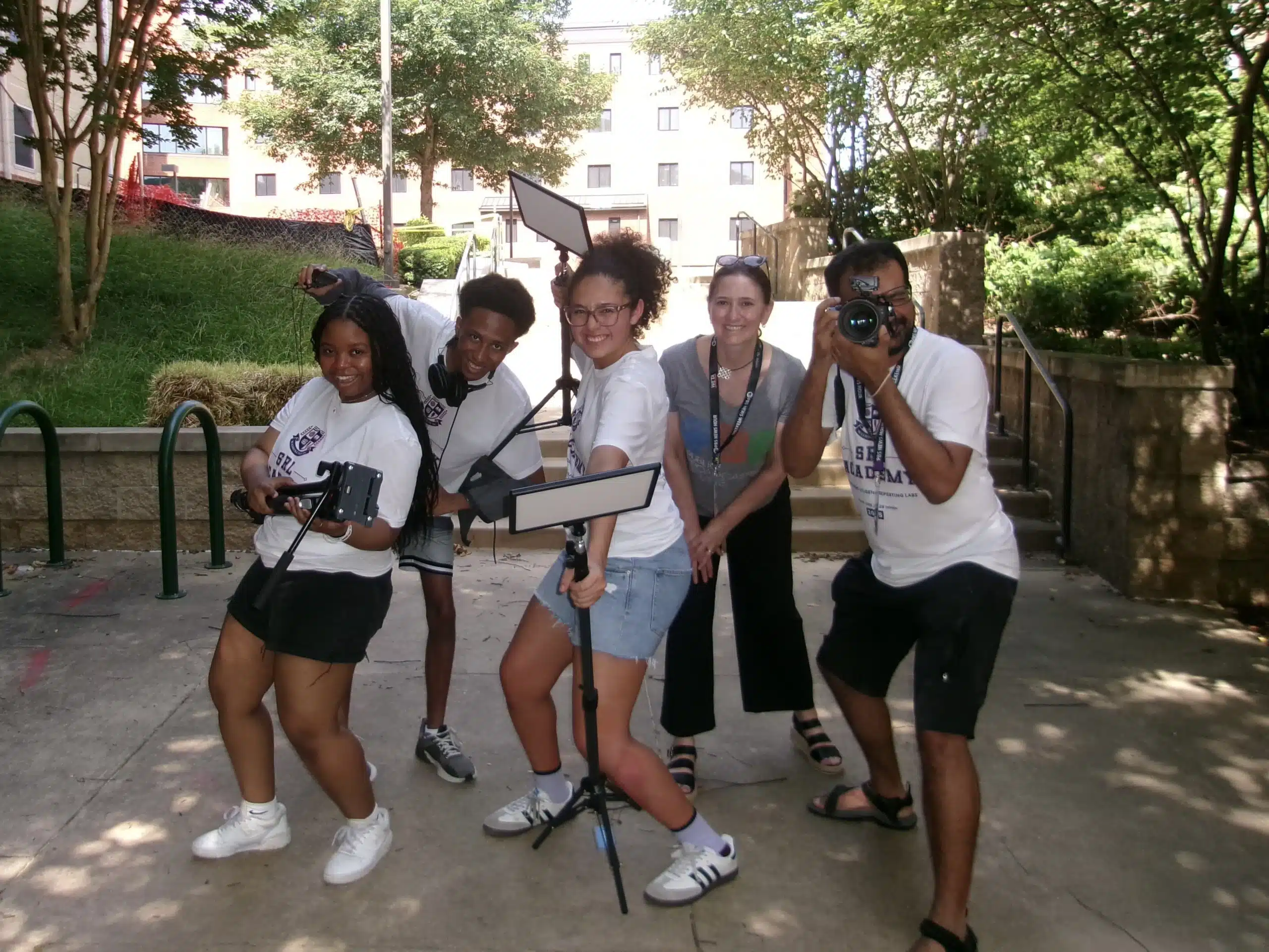 Three high school students and two adults hold broadcast equipment while posing for a photo